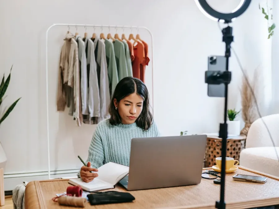 Online fashion seller preparing an Ajio catalog on a laptop beside a clothing rack